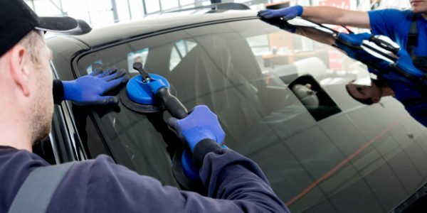 Automobile special workers replacing windscreen or windshield of a car in auto service station garage.